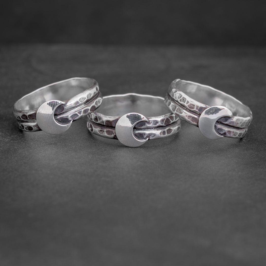 A group of handmade sterling silver witch rings. They have a silver crescent moon on a hammered ring band. Art jewelry made in Fort Collins, Colorado.