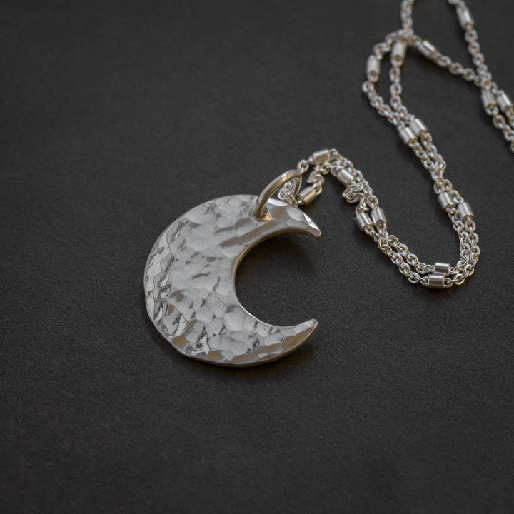 A silver witch necklace featuring a hammered crescent moon on a sterling silver chain.